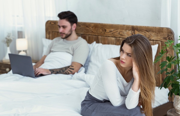 woman sitting on bed and looking at man, texting on laptop
